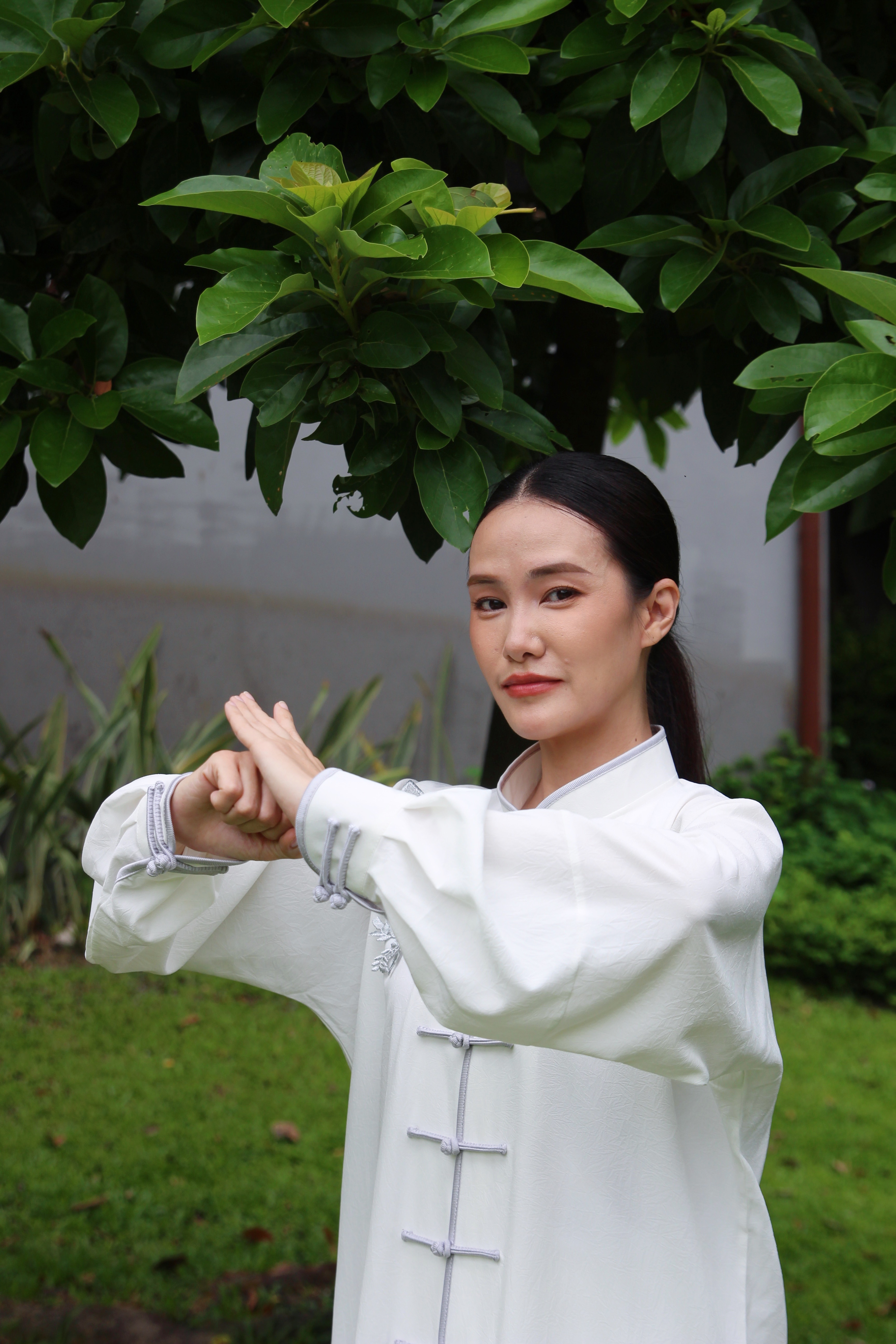 Master Julie practicing Qigong outdoors in a white traditional uniform, hands held in a flowing posture.