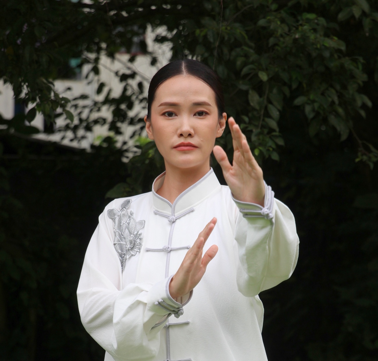 Close portrait of Master Julie in a white Qigong uniform, hands held with quiet precision, illustrating the details of posture and movement.